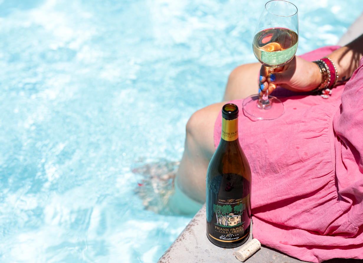 Image shows woman with her feet in the pool drinking wine from Frank Family Vineyards