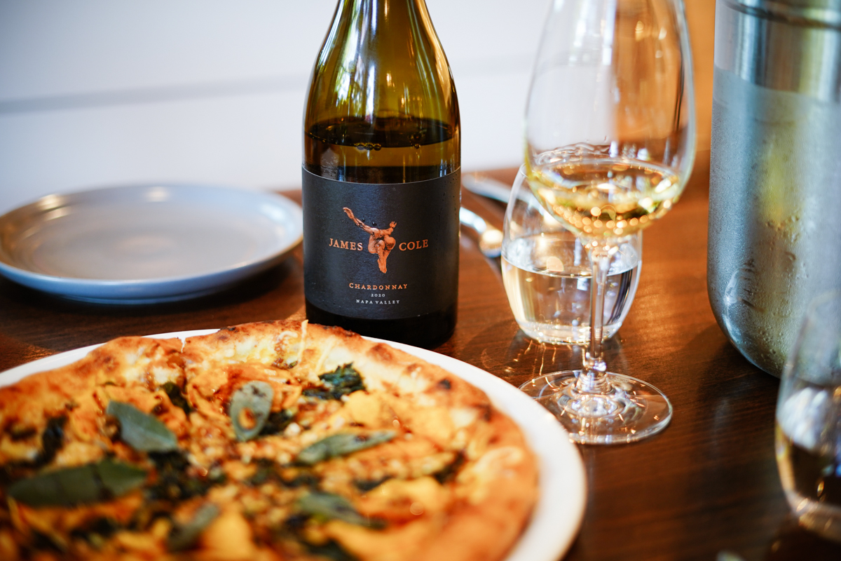 image shows a pizza and a bottle of wine from James Cole Winery