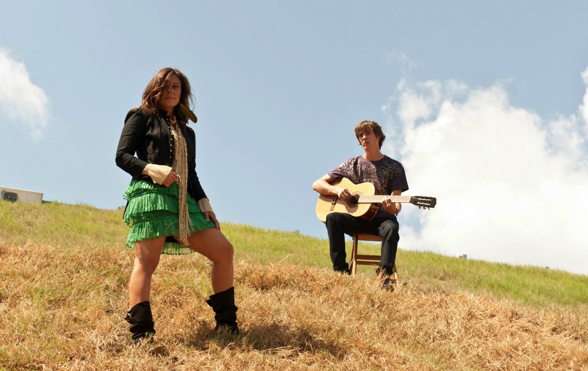 Man and woman standing on a hill. Man is holding a guitar.