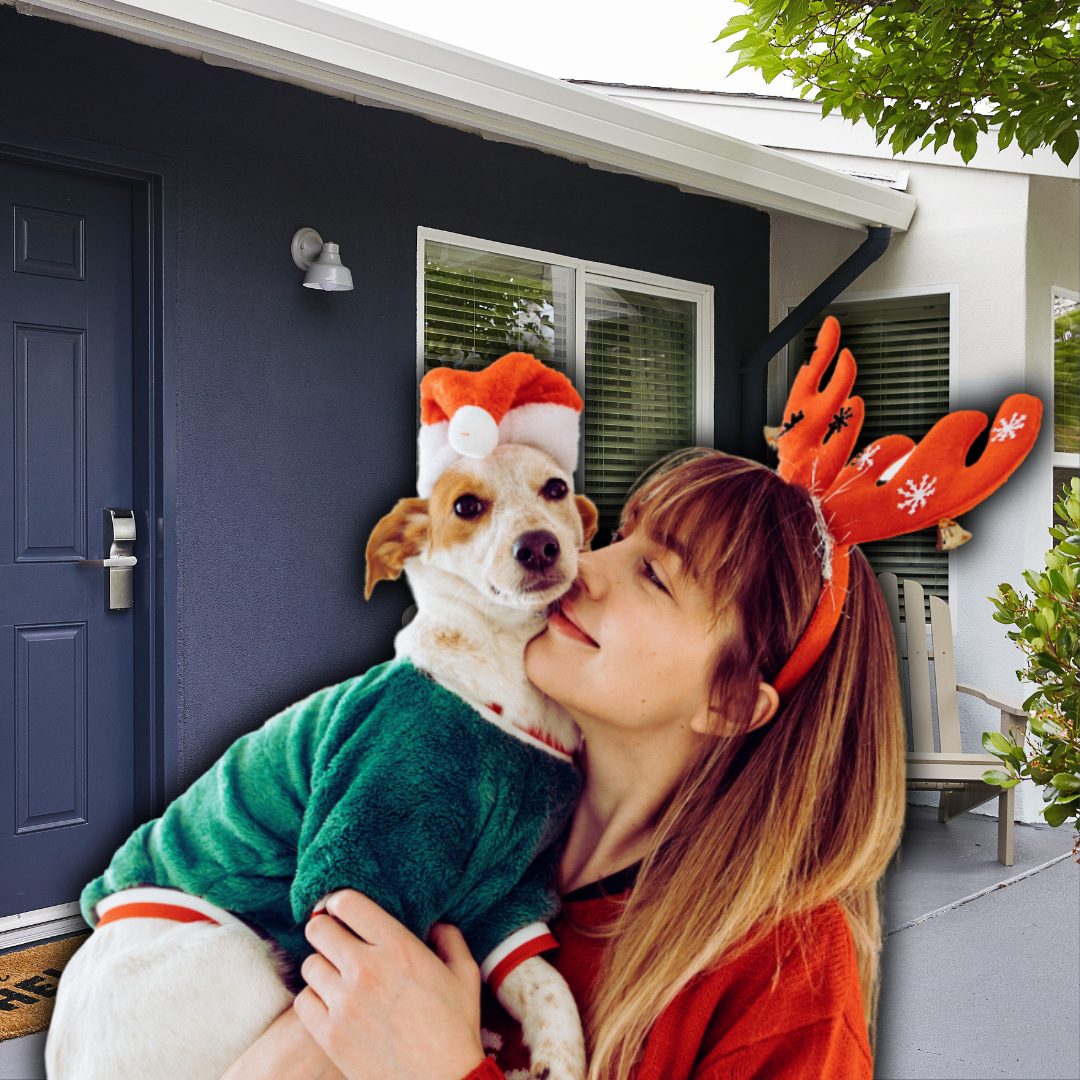 woman wearing reindeer antlers holding a dog in a sweater and santa hat