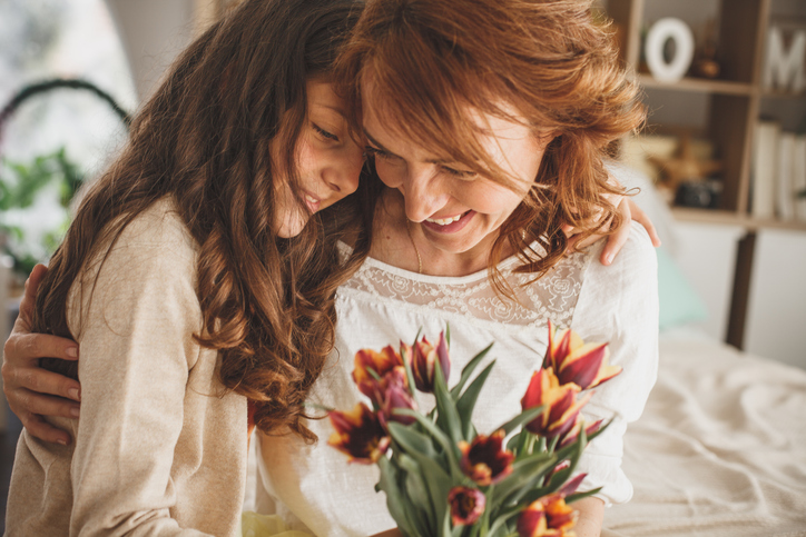mom and daughter hugging with a bouquet of flowers
